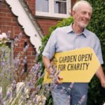 A man holding a garden open sign for National Garden Scheme